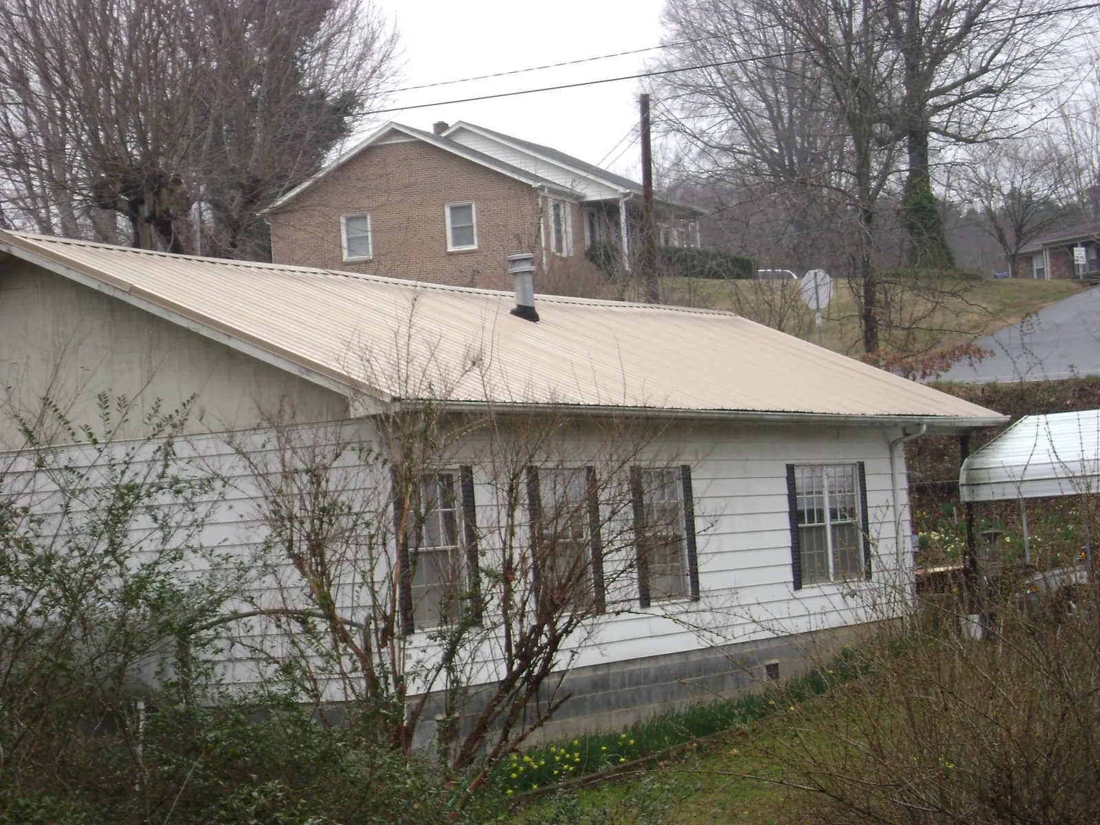 Tan metal roof on a white sided house set into a hillside — Commercial Roofing by Roofing Brothers in Berwick